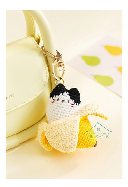 Un Pequeño Bolso Amarillo Con Un Llavero Adjunto Que Presenta Un Lindo Diseño De Cáscara De Plátano Tejida a Crochet Con Una Sección Parcialmente Pelada Que Revela Una Figura Tejida a Crochet En Blanco Y Negro En El Interior El Fondo Incluye Sutiles Toques De Ilustraciones De Frutas