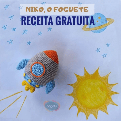 Un cohete tejido a crochet con un cuerpo gris, aletas azules y una punta naranja se encuentra sobre un fondo dibujado a mano de un cielo soleado con estrellas, un planeta y el sol. El texto en la parte superior dice "Niko, o Foguete Receita Gratuita" y "angatu" es visible cerca de la parte inferior. Ideal para aquellos interesados en cómo hacer amigurumi.