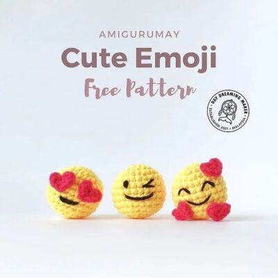 Tres emojis amarillos tejidos a crochet con diferentes expresiones se sientan sobre un fondo claro. Un emoji tiene ojos de corazón, el emoji del medio hace un guiño y el tercer emoji tiene una cara sonriente con corazones en las mejillas. El texto dice "Patrón gratuito de emojis lindos de Amigurumay".