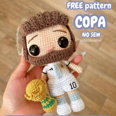 Una mano sostiene un muñeco de crochet de un jugador de fútbol que viste una camiseta celeste y blanca con el número 10, con un pequeño trofeo al lado. El texto de la imagen dice: "Patrones GRATIS COPA NO SEW @STUDIOGURUMI. Encuentra patrones gratis de amigurumi en español.