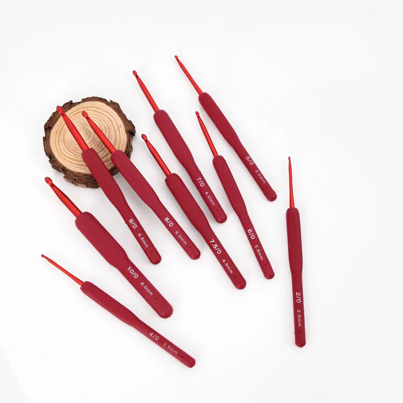 Un Conjunto De Diez Agujas De Crochet Rojas De Diferentes Tamaños Están Dispuestas En Forma De Abanico Sobre Una Superficie Blanca Cada Gancho Tiene Una Etiqueta De Tamaño En Milímetros Inscrita En El Mango Un Pequeño Disco De Madera Se Encuentra Cerca De La Parte Superior Izquierda Y Agrega Un Elemento Decorativo a La Exhibición