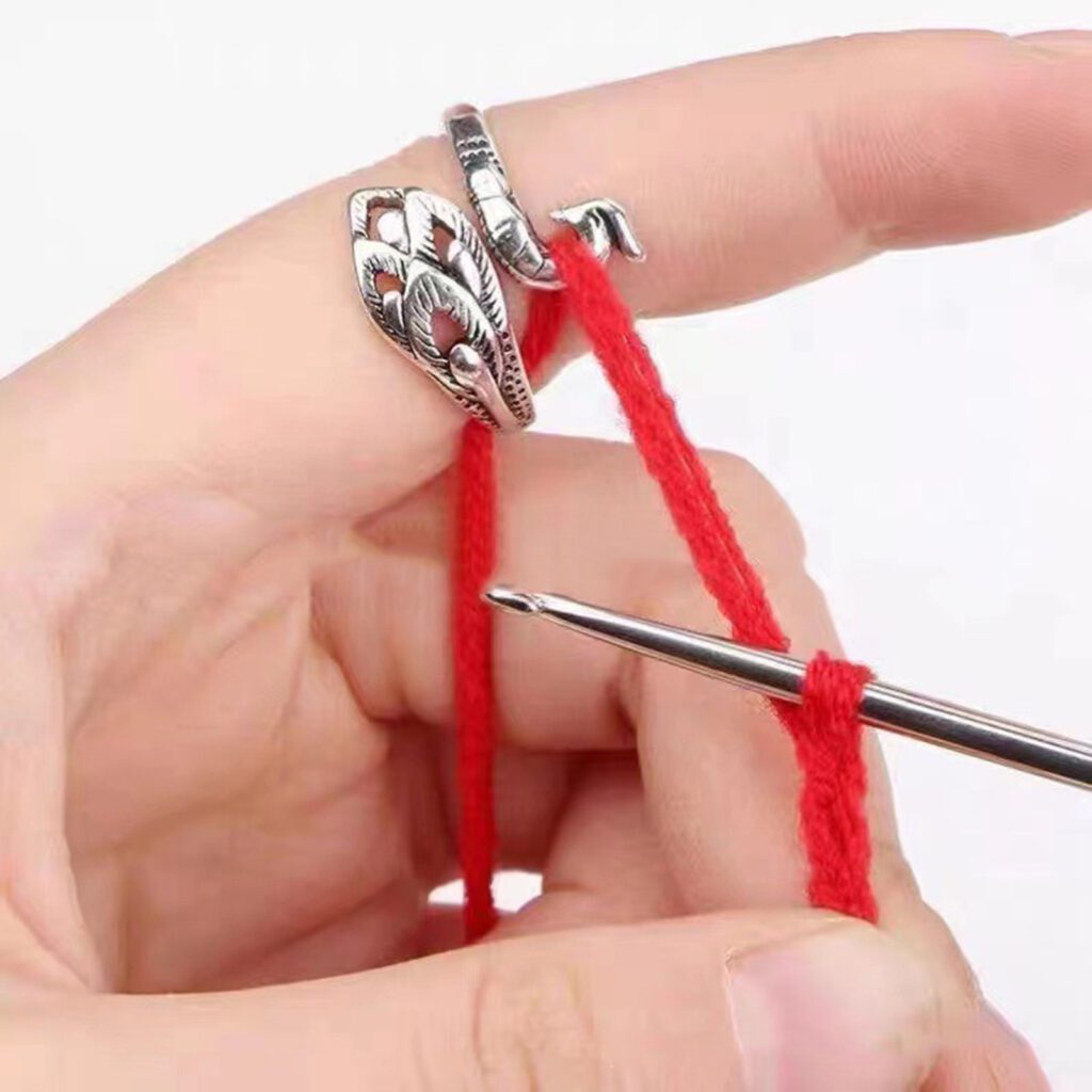 Primer Plano De Una Mano Tejiendo Con Hilo Rojo La Mano Adornada Con Anillos Plateados Sostiene Un Ganchillo De Metal Con El Hilo Enrollado Alrededor Listo Para Ser Trabajado Los Dedos Están Colocados Para Guiar El Hilo Suavemente a Través Del Proceso De Crochet