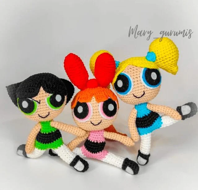 Tres Muñecas De Crochet Que Representan a Las Chicas Superpoderosas Con Blossom centro Bubbles derecha Y Buttercup izquierda Están Vestidos Con Sus Colores Característicos verde Rosa Y Azul Y Adoptan Una Pose Divertida Con Una Pierna Levantada El Fondo Es Blanco Con El Nombre mary Gunumis Escrito En La Esquina