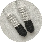 Dos Pequeños Objetos De Crochet Que Se Asemejan a Calcetines Blancos Y Negros En Miniatura Se Colocan Uno Al Lado Del Otro Sobre Un Fondo Gris Texturizado Que Recuerda Al Icónico Traje De Batman La Parte Superior Es Blanca Y La Parte Inferior Pasa a Ser Negra