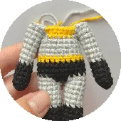 Una Foto De Primer Plano De Una Pequeña Figura De Batman Tejida a Crochet La Figura Tiene Un Traje a Rayas En Colores Gris Amarillo Y Negro Se Ve Una Mano Que Sostiene La Figura Lo Que Sugiere El Tamaño Y Los Detalles Intrincados Del Trabajo De Crochet La Figura De Batman Parece Estar En Progreso Ya Que Todavía Hay Hilos De Hilo Unidos