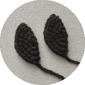 Una Imagen De Primer Plano De Dos Objetos En Forma De Almendra De Ganchillo Negro Sobre Un Fondo Con Textura Gris Claro Los Objetos Que Recuerdan a La Capucha De Batman Presentan Patrones Intrincadamente Tejidos Y Colas Alargadas Que Se Extienden Desde Su Base