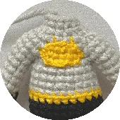 Un Suéter De Crochet Gris Con Un Diseño De Sol Amarillo En El Pecho Y Un Patrón Amarillo Y Negro Inspirado En Batman Alrededor Del Dobladillo Inferior El Jersey Se Presenta Sobre Un Fondo Liso Y De Color Claro