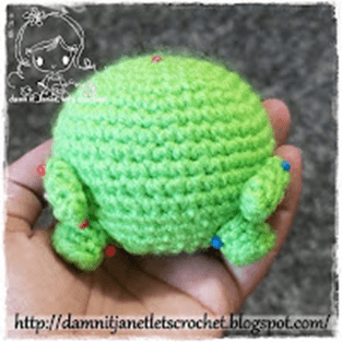 Una Mano Sostiene Una Criatura Pequeña Redonda De Ganchillo Verde Con Extremidades Diminutas Que Recuerda a Mike Wazowsky El Fondo Es Borroso Centrando La Atención En El Lindo Artículo Hecho a Mano La Url Del Blog Es Visible En La Parte Inferior Httpdamnitjanetletscrochetblogspotcom