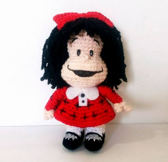 Una Muñeca De Crochet Con Pelo Negro Un Vestido Rojo Con Cuello Blanco Y Zapatos Negros Con Una Amplia Sonrisa Y Un Lazo Rojo En El Pelo Esta Encantadora Creación Se Parece Al Clásico Personaje De Dibujos Animados Mafalda