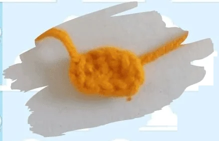 Un Pequeño Objeto De Color Naranja Tejido a Crochet En Forma De Riñón Con Dos Extremos De Hilo Que Sobresalen Descansa Sobre Un Fondo Blanco Adornado Con Diseños De Nubes De Madera