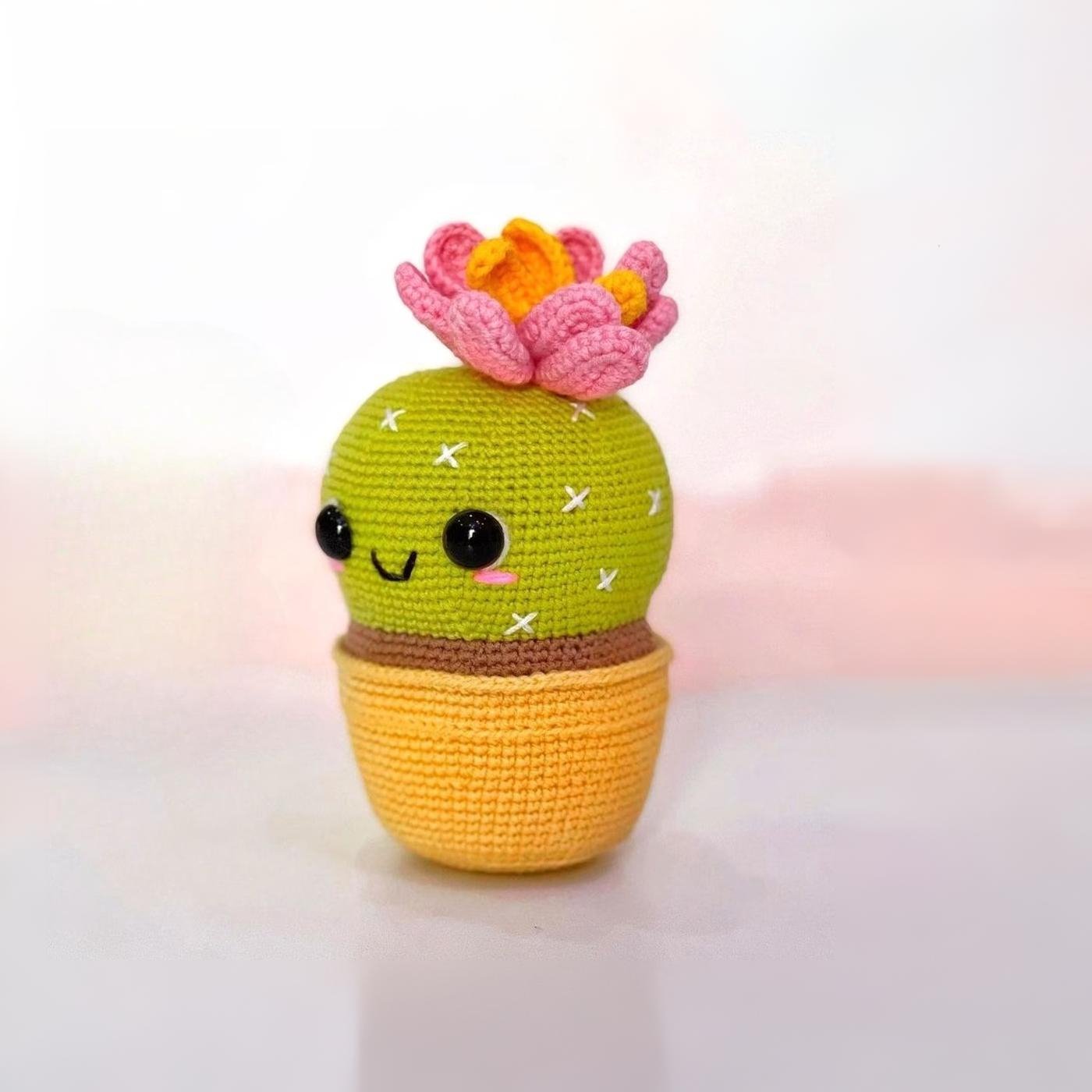 Adorable cactus amigurumi tejido a crochet con una maceta amarilla y una flor rosa, sonriendo.