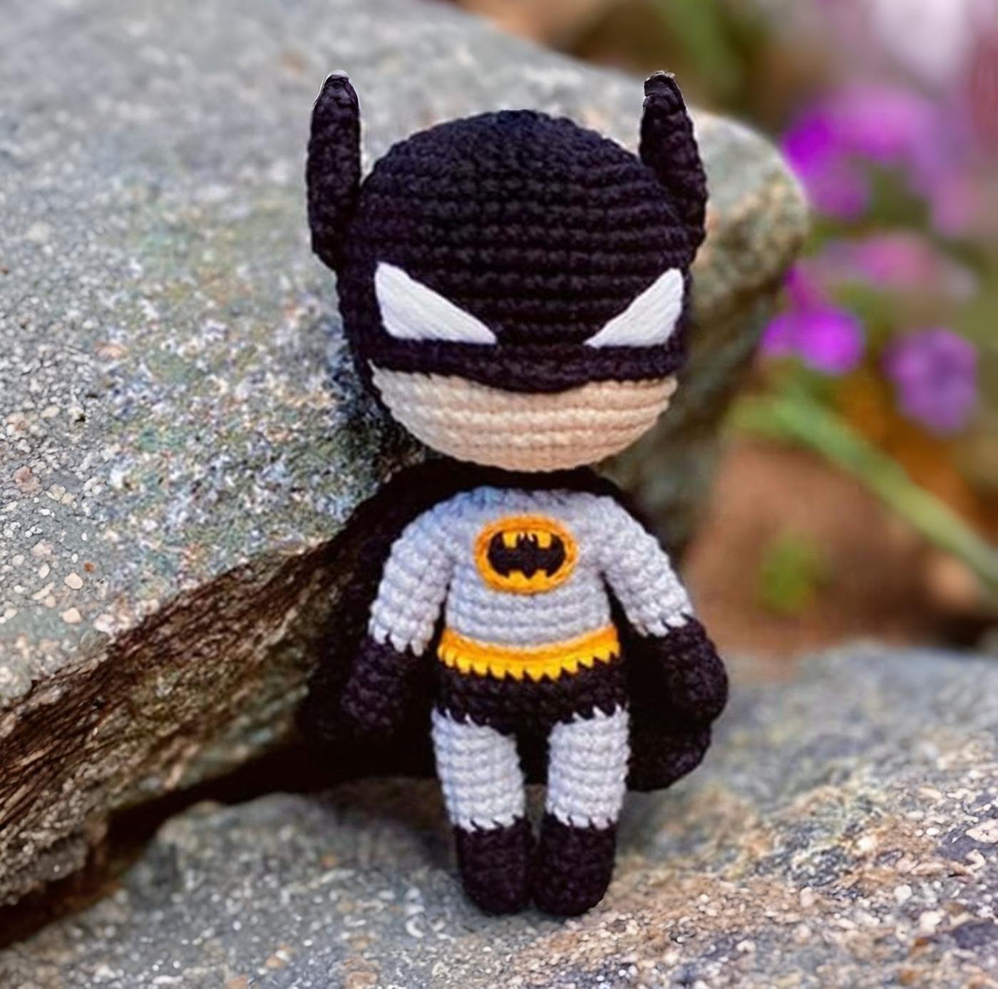 Muñeco amigurumi de Batman tejido a ganchillo, de pie sobre un fondo neutro.