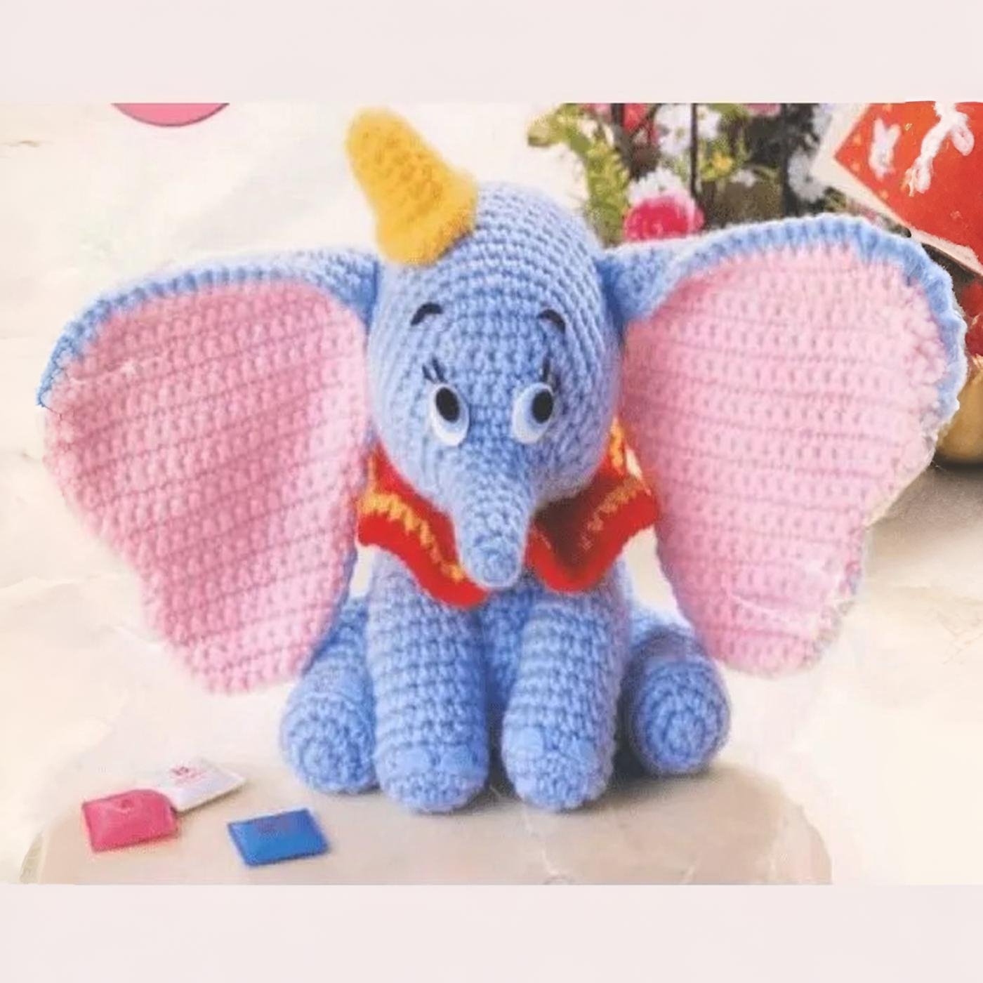 Amigurumi de Dumbo tejido a crochet, mostrando sus grandes orejas rosadas y su gorro amarillo.