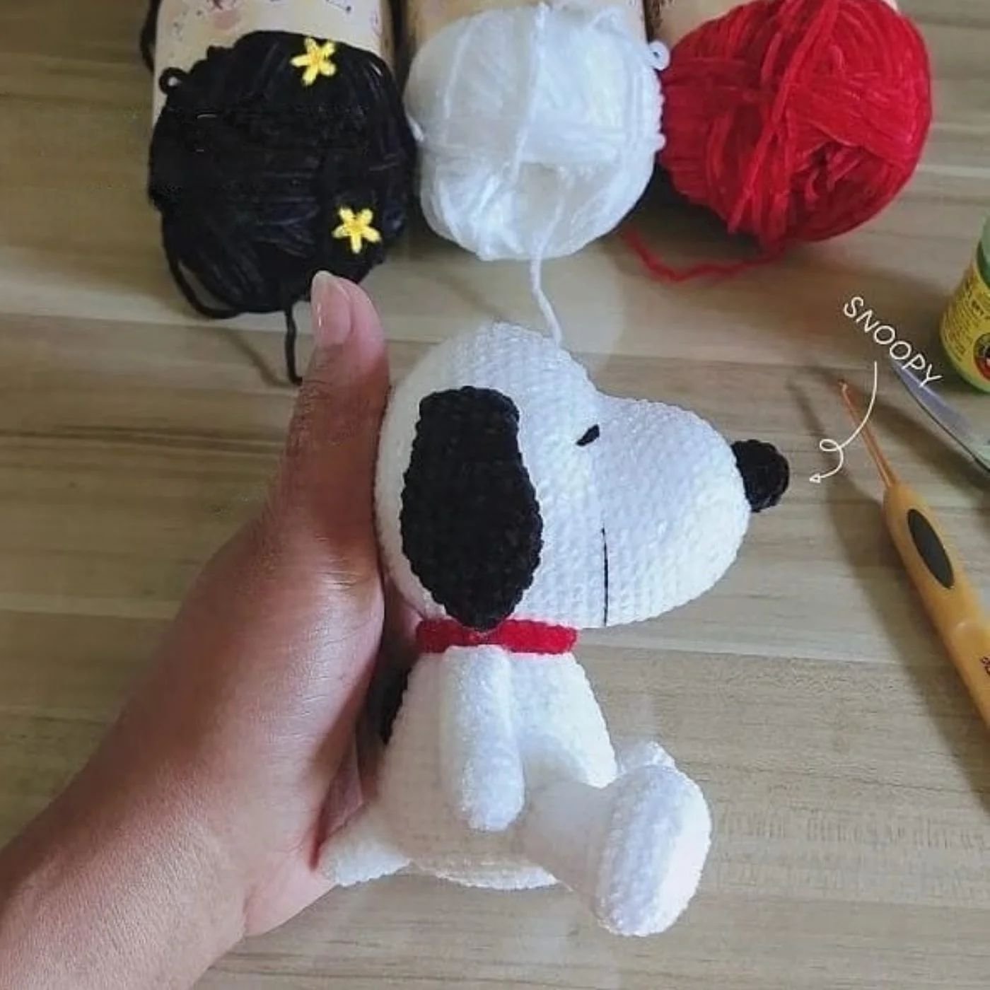 Grupo de muñecos amigurumi de Snoopy tejidos a crochet sentados sobre superficie de madera, mostrando detalles de orejas negras y collar rojo