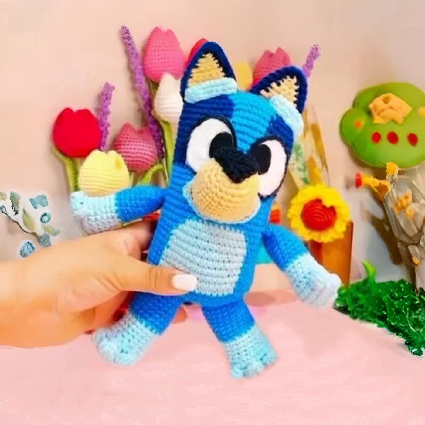 Muñeco amigurumi de Bluey tejido a ganchillo, posando sobre un fondo blanco
