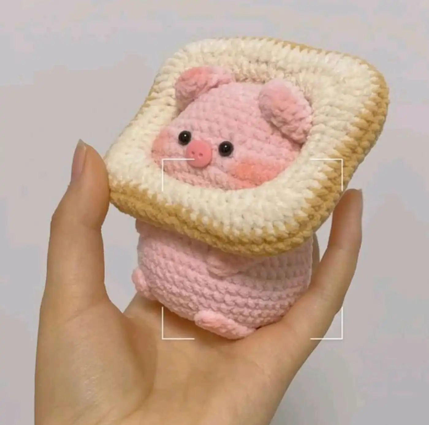 Adorable cerdito amigurumi tejido a crochet descansando dentro de un panecillo, hecho a mano con hilo suave
