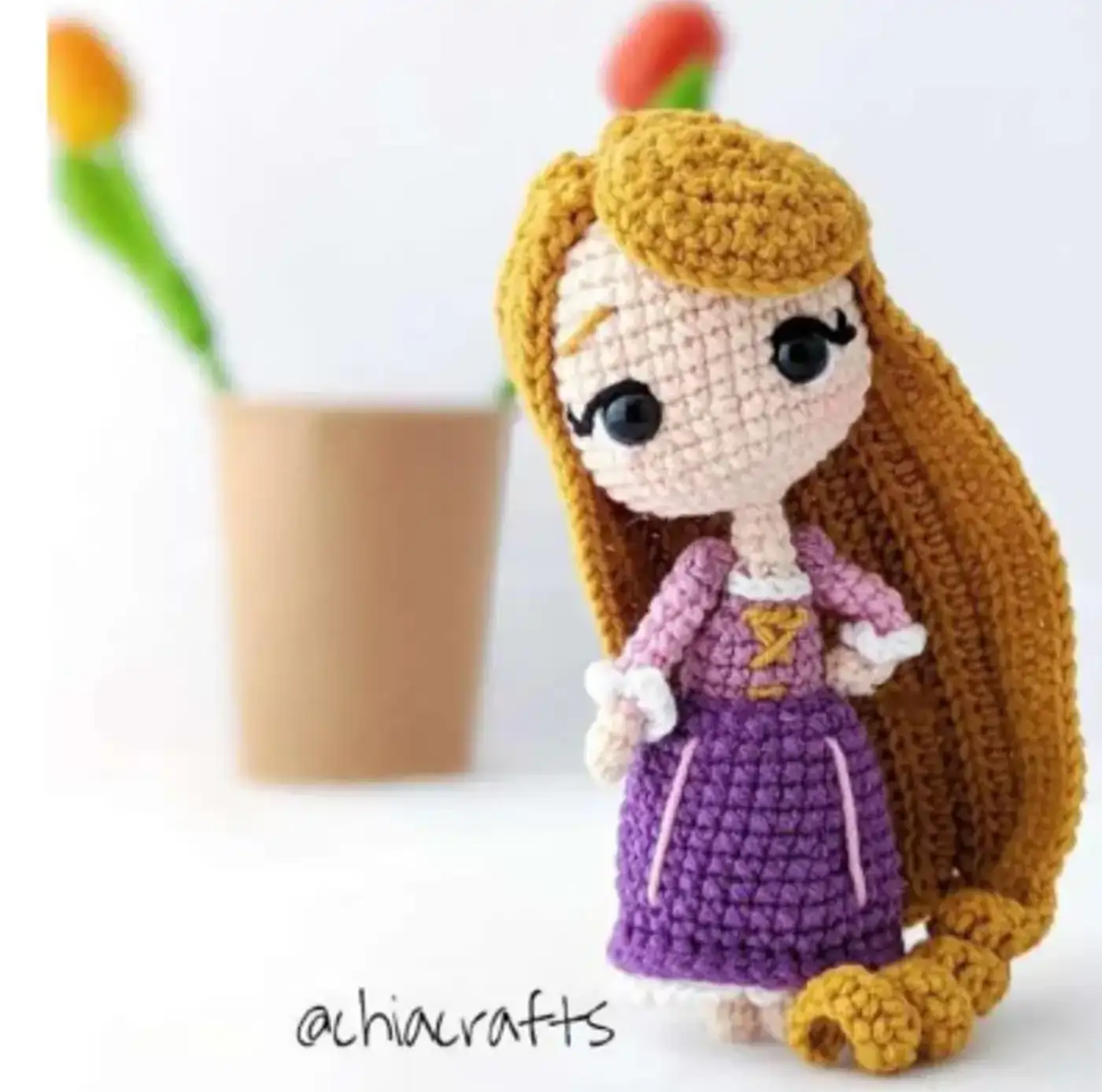 Muñeca Rapunzel amigurumi terminada, con su largo cabello rubio y vestido morado, sobre un fondo blanco.
