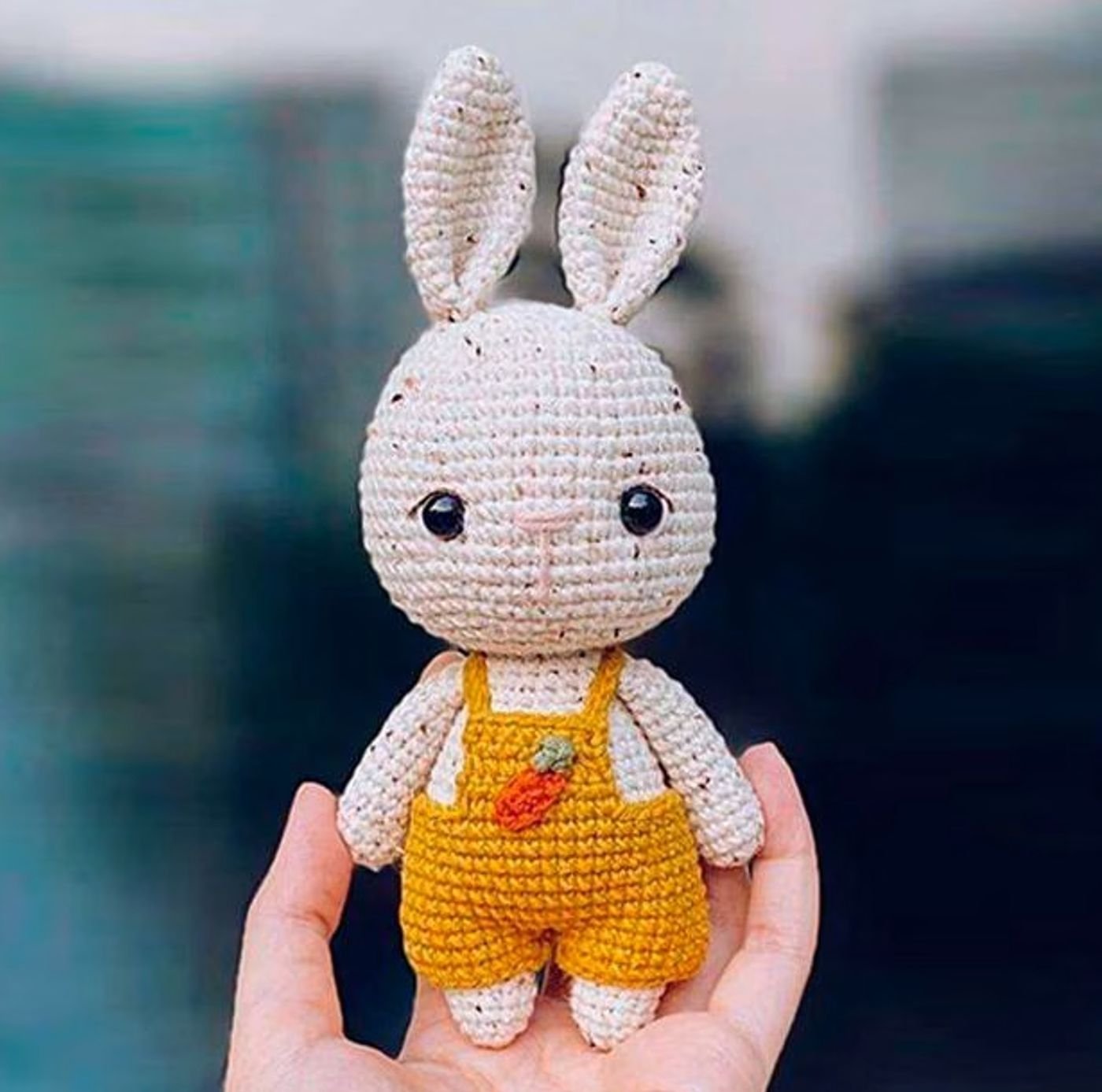Conejo amigurumi tejido a ganchillo llamado Avellana, sentado y vestido con un overol marrón.