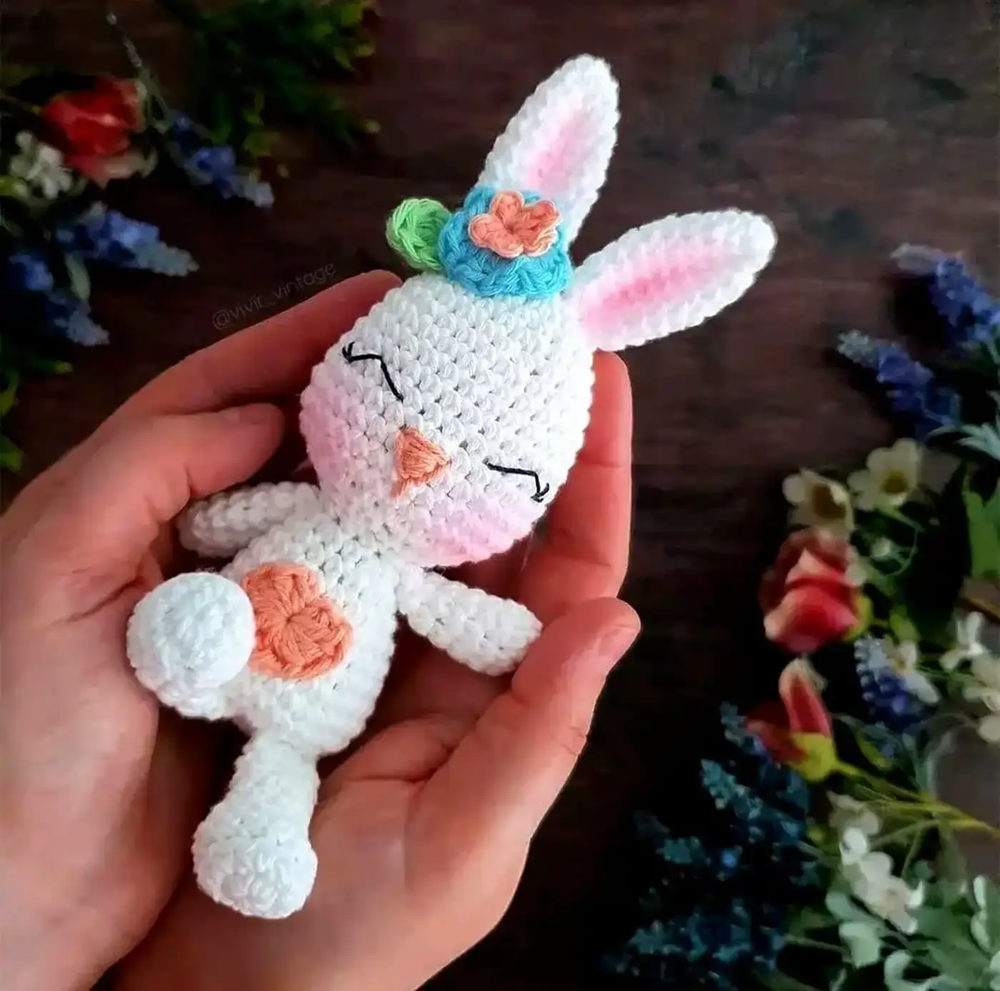 Conejo Amigurumi Adelfa terminado, de color blanco con detalles florales, sentado sobre una superficie clara.