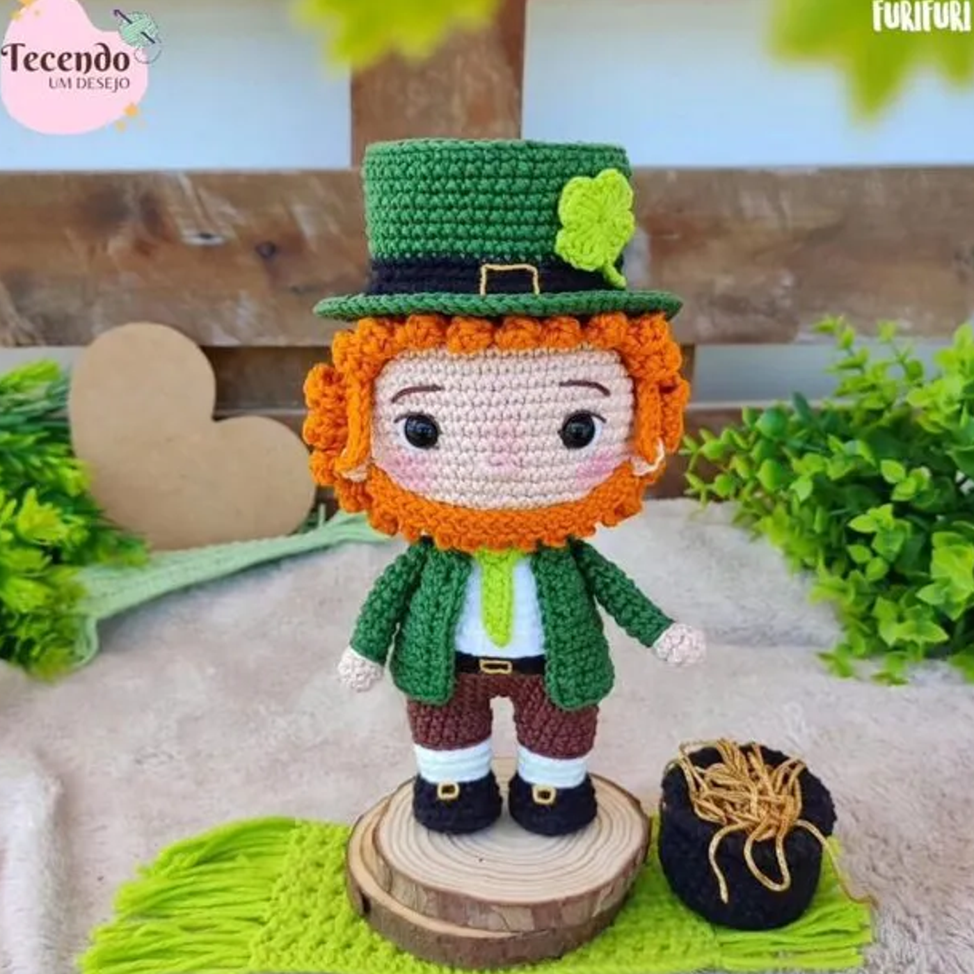 Duende de la fortuna amigurumi tejido a ganchillo con sombrero verde, traje marrón y barba naranja, sosteniendo un caldero.