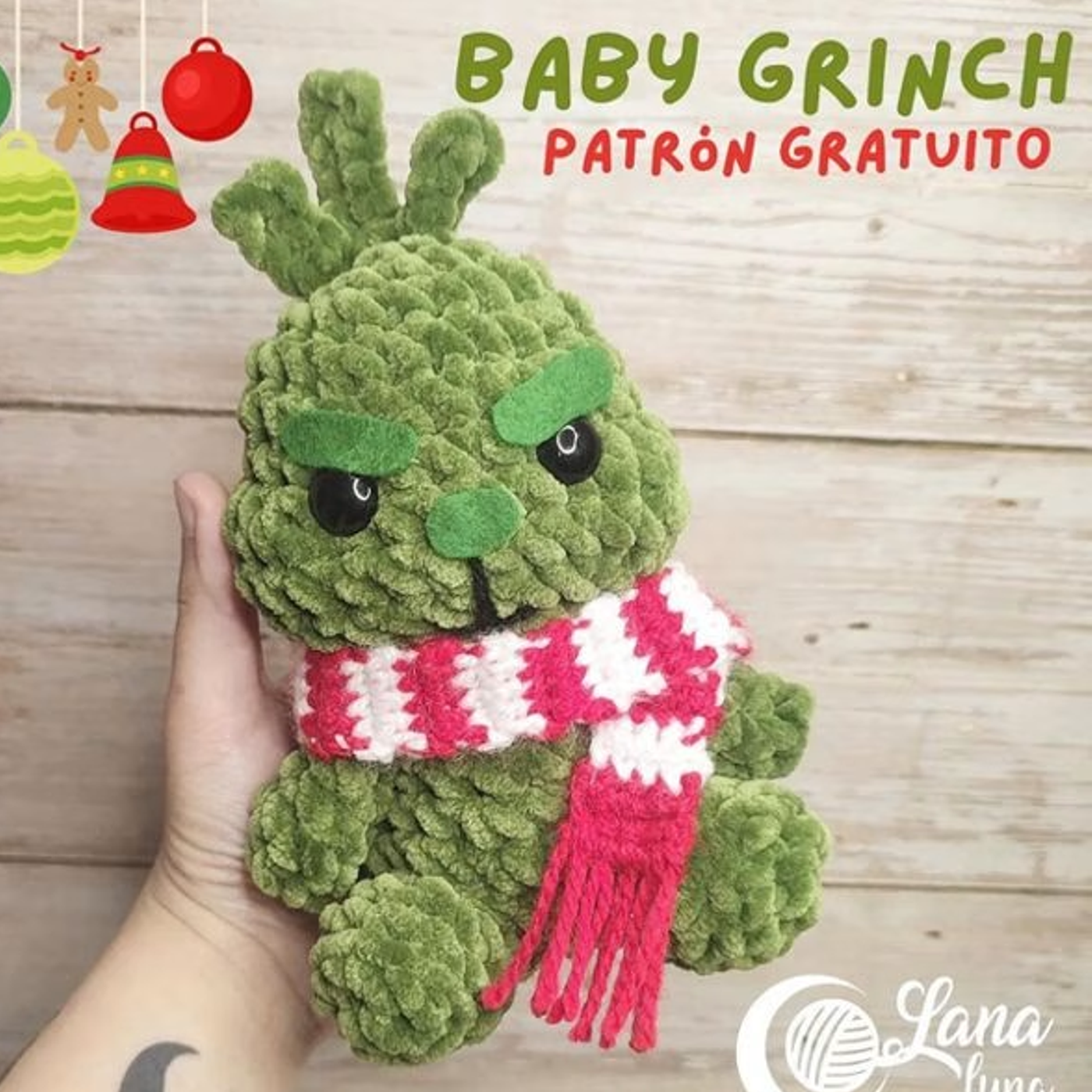 Muñeco tejido del Grinch bebé amigurumi terminado, con su bufanda roja y blanca, sentado sobre un fondo blanco.