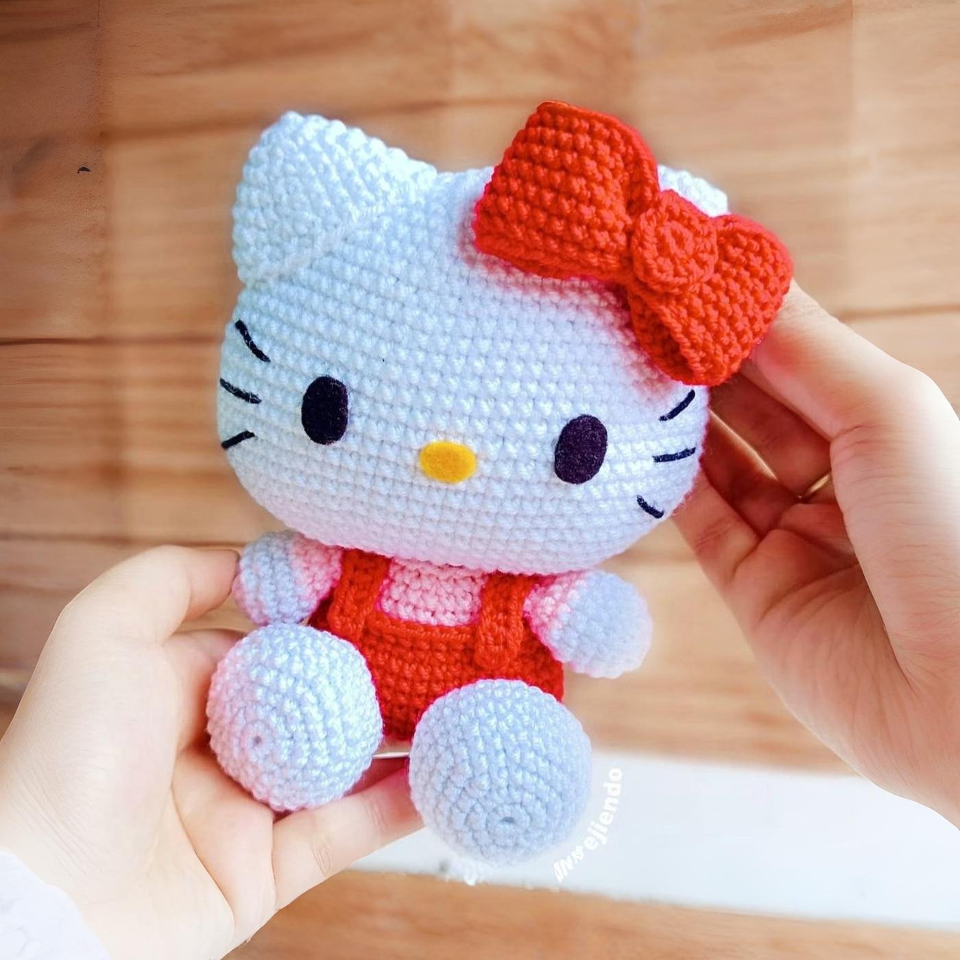 Muñeco de Hello Kitty amigurumi tejido a crochet, sentado sobre un fondo claro.