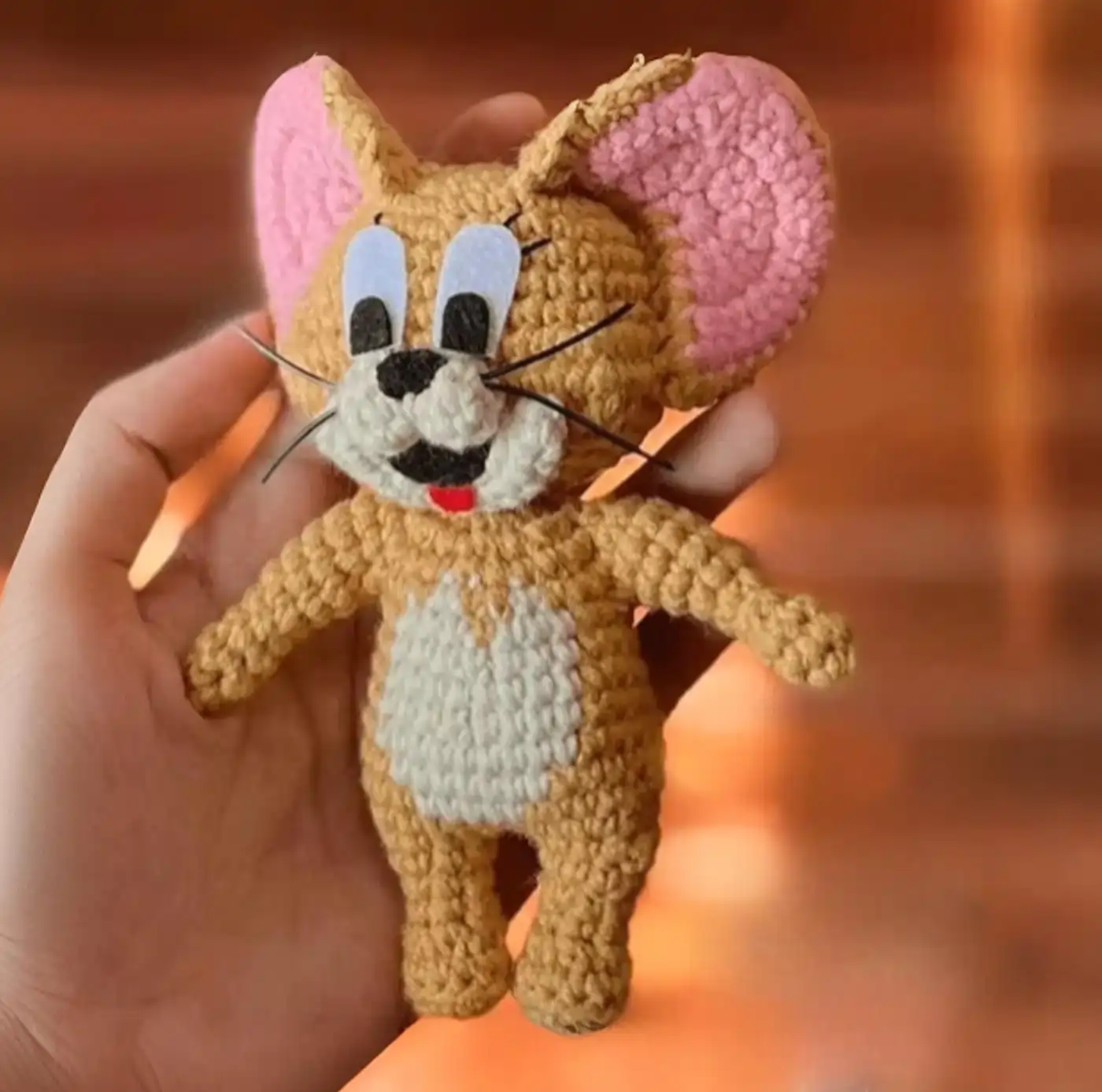 Muñeco de Jerry amigurumi terminado, tejido a crochet, sentado sobre una superficie de madera.