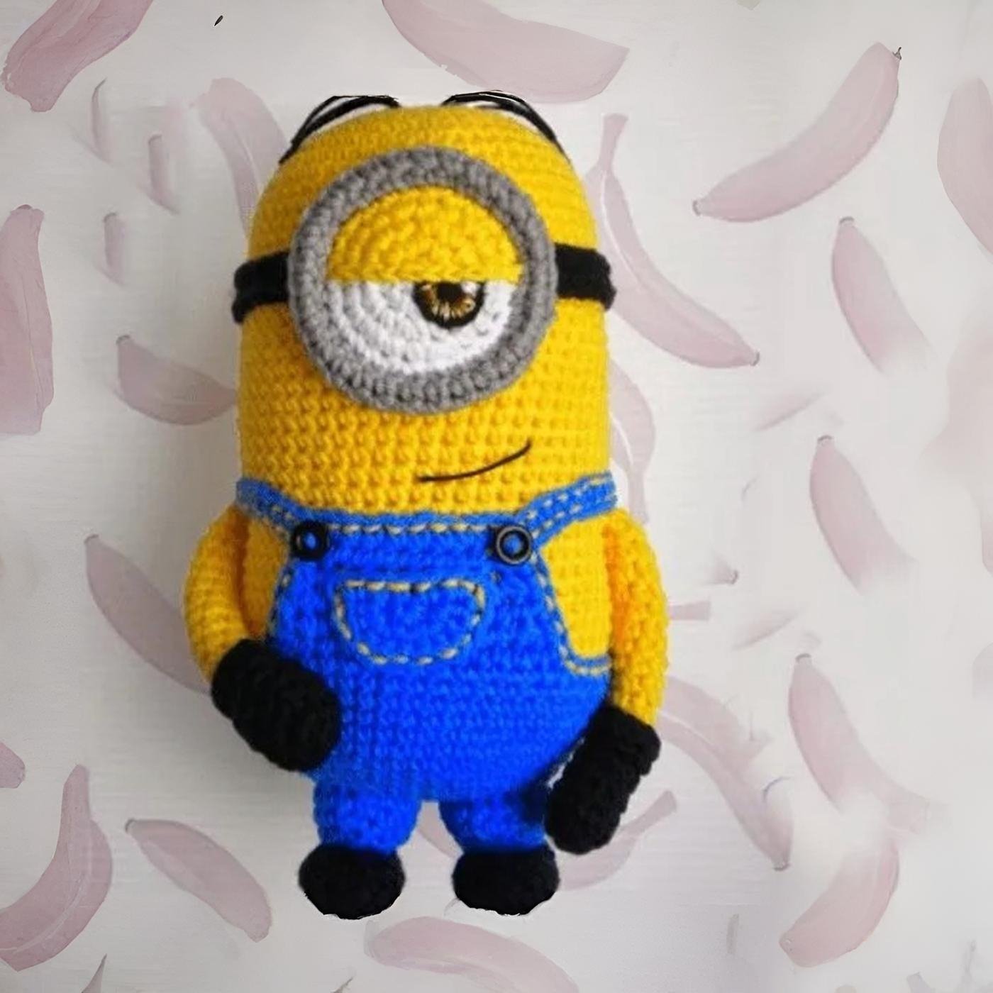 Muñeco amigurumi de Stuart el Minion tejido a ganchillo, de pie sobre un fondo blanco.