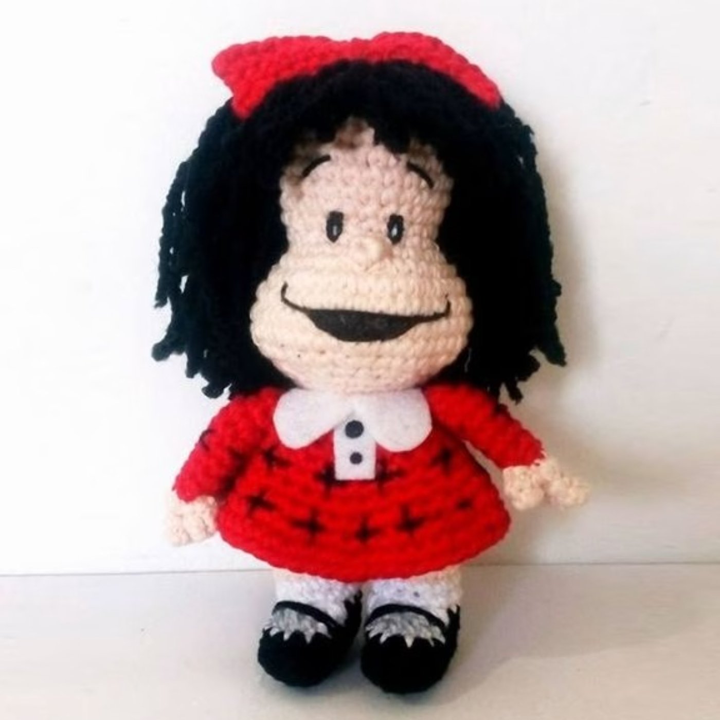 Muñeco amigurumi de Mafalda terminado, tejido a ganchillo con su vestido rojo y moño característico.