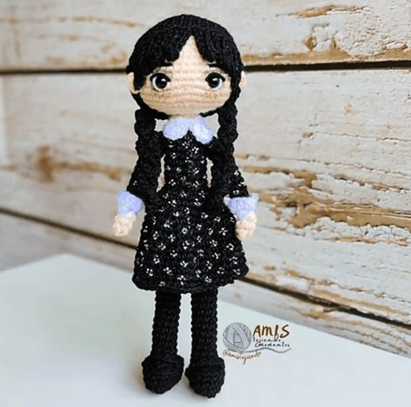 Muñeca amigurumi de Merlina Addams tejida a ganchillo con su vestido negro y trenzas características.