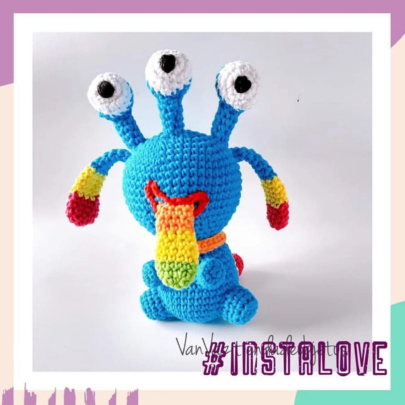 Monstruo amigurumi colorido tejido a crochet, de color turquesa con tres ojos, una gran sonrisa y detalles en fucsia, amarillo y naranja.