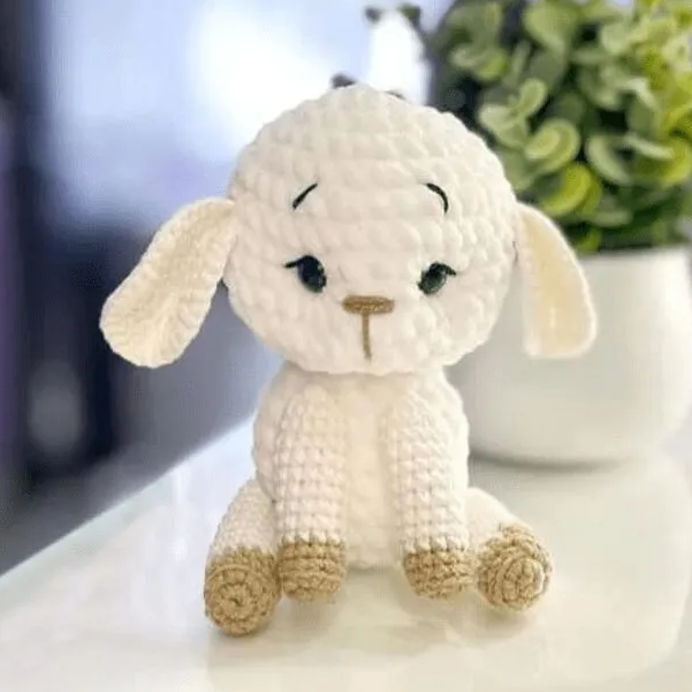 Ovejita amigurumi tejida a crochet sentada sobre una superficie de madera, mostrando su textura suave y detalles bordados.
