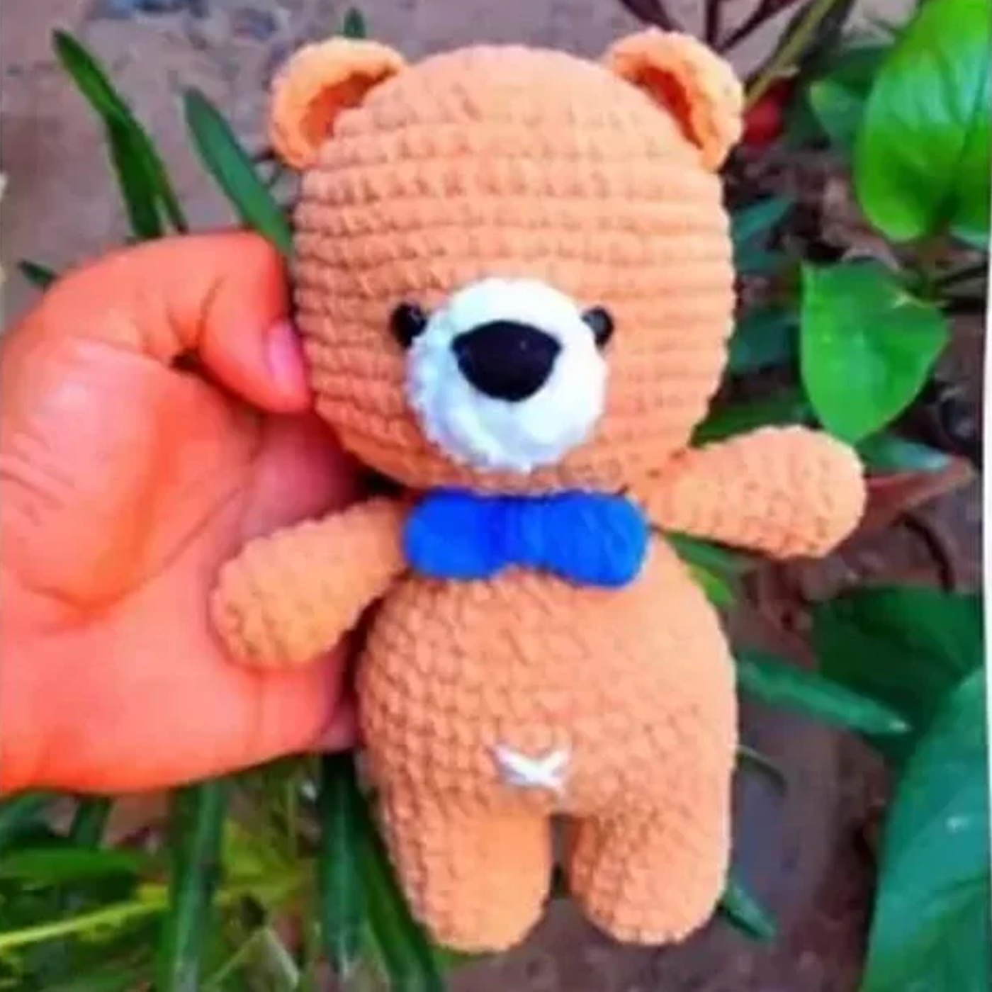Oso teddy amigurumi terminado, tejido a ganchillo con lana marrón y una corbata azul, sobre un fondo claro.
