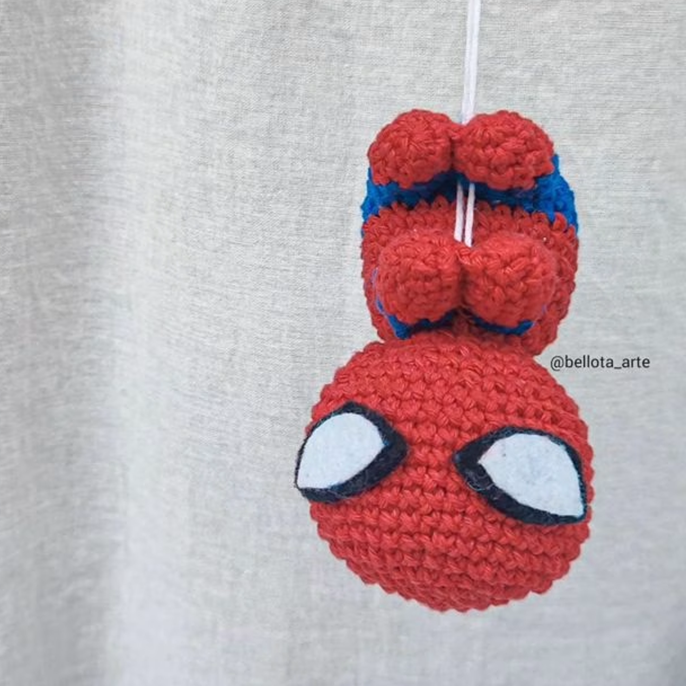 Muñeco amigurumi de Spiderman colgando de su telaraña, tejido a ganchillo con los colores rojo y azul característicos.