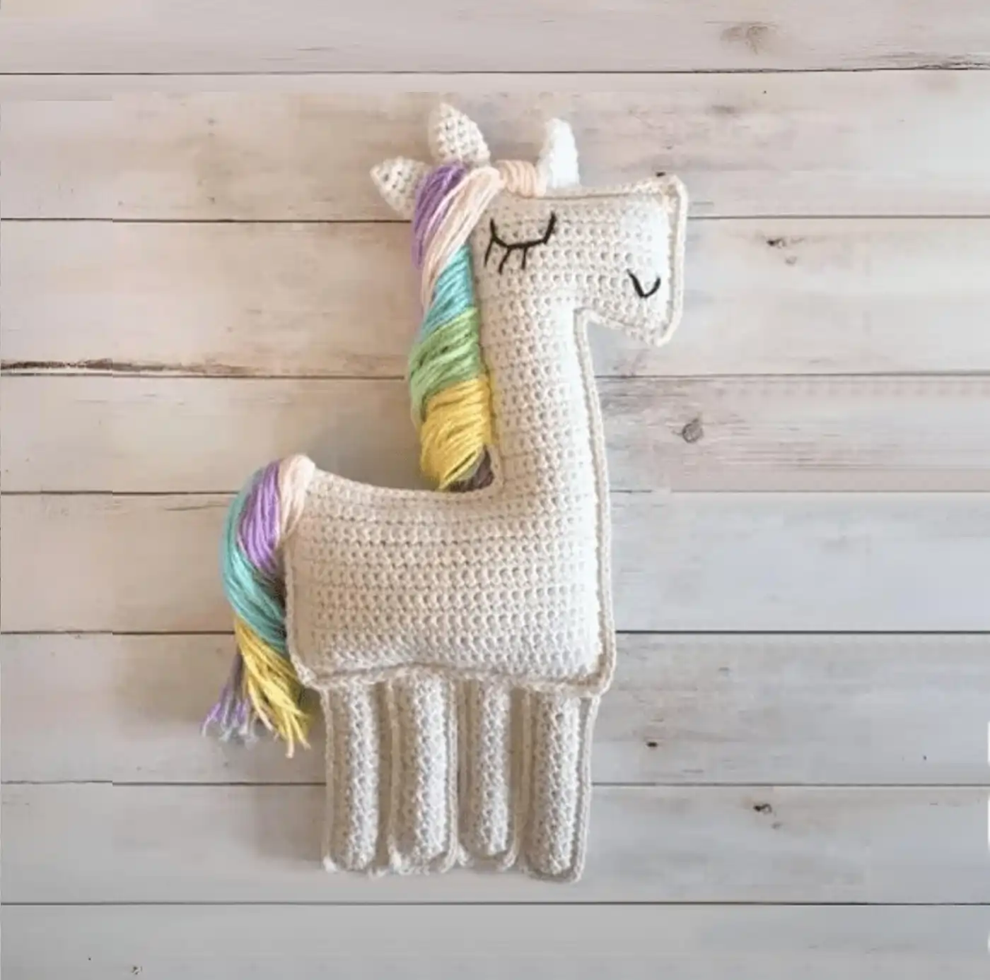 Unicornio tejido a crochet estilo Ragdoll con melena de colores pastel y cuerpo plano, vista frontal completa