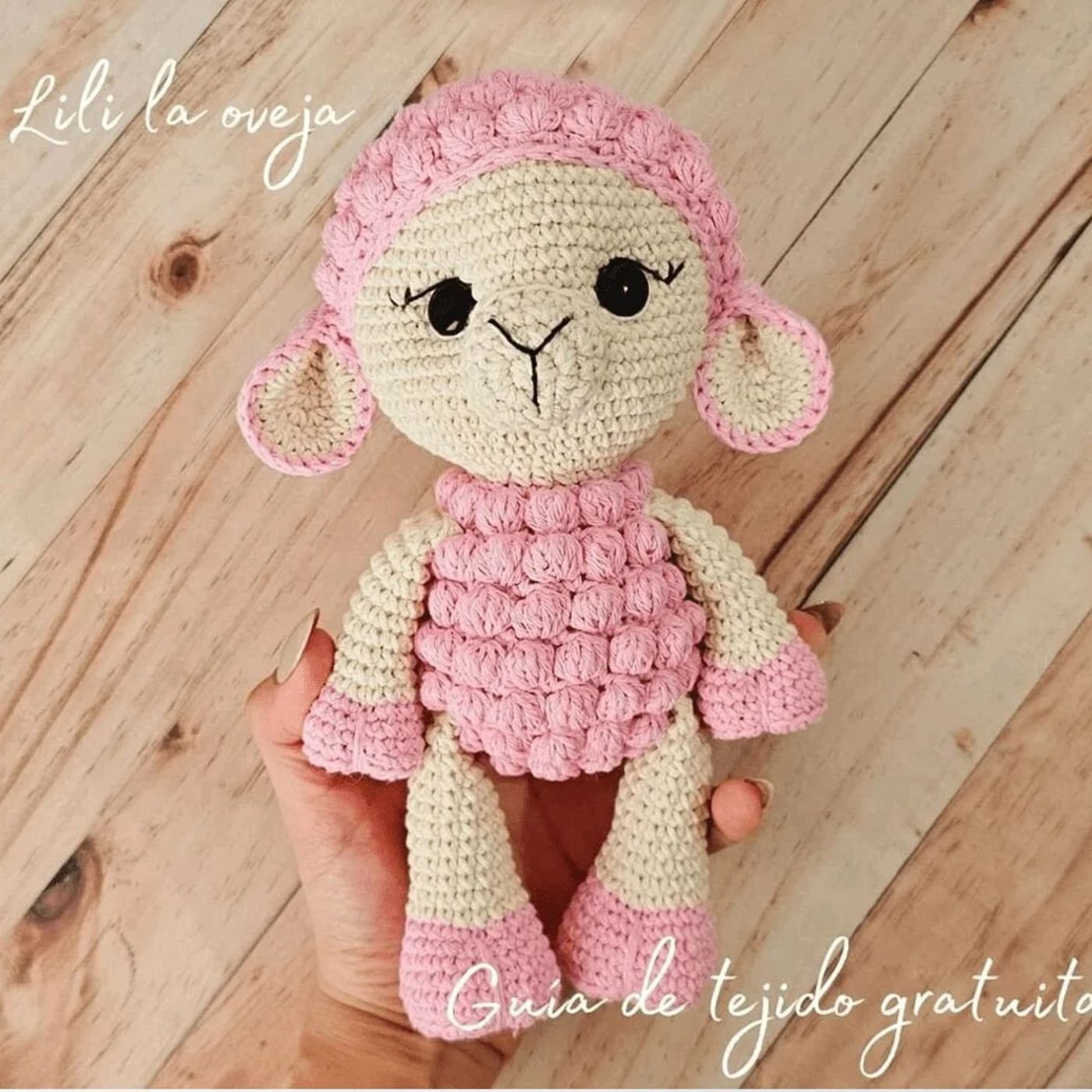 Oveja amigurumi terminada, tejida con lana rosa y cruda, sentada sobre un fondo claro.