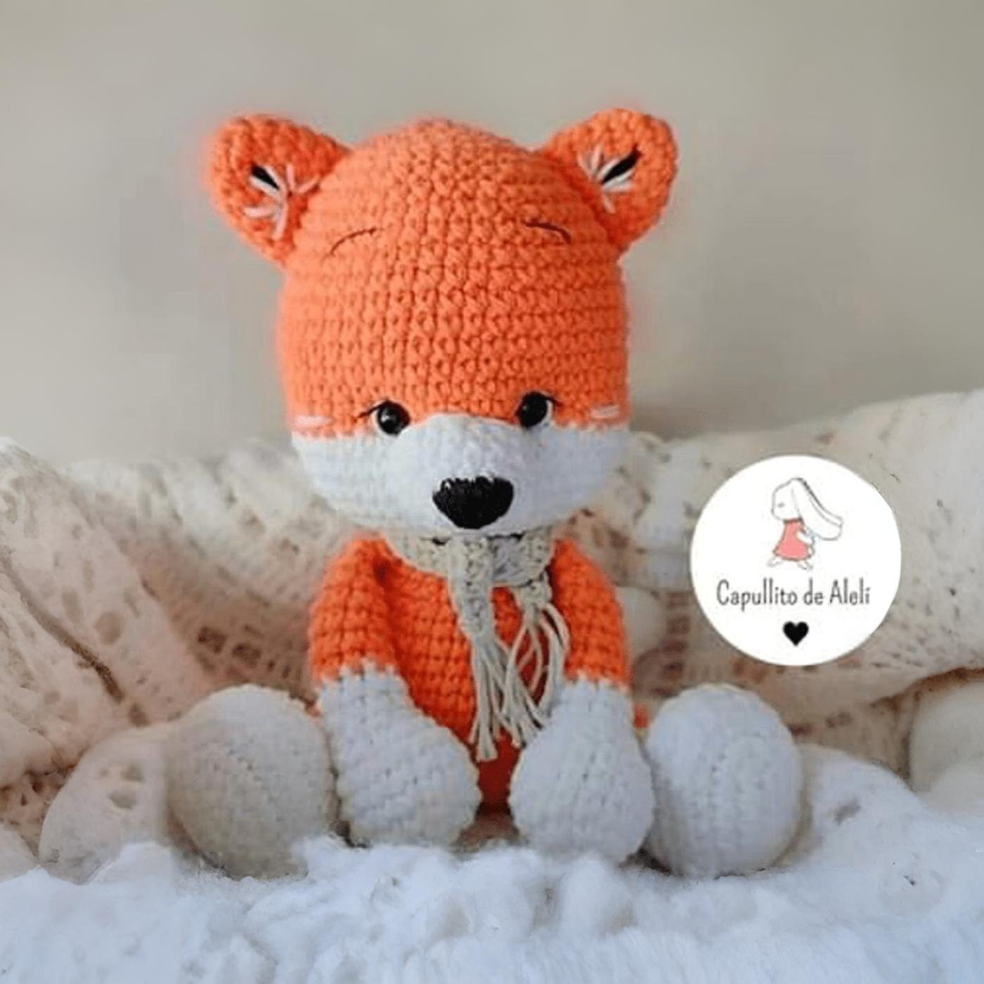 Zorro amigurumi Renzo tejido a crochet con bufanda gris, sentado sobre fondo claro