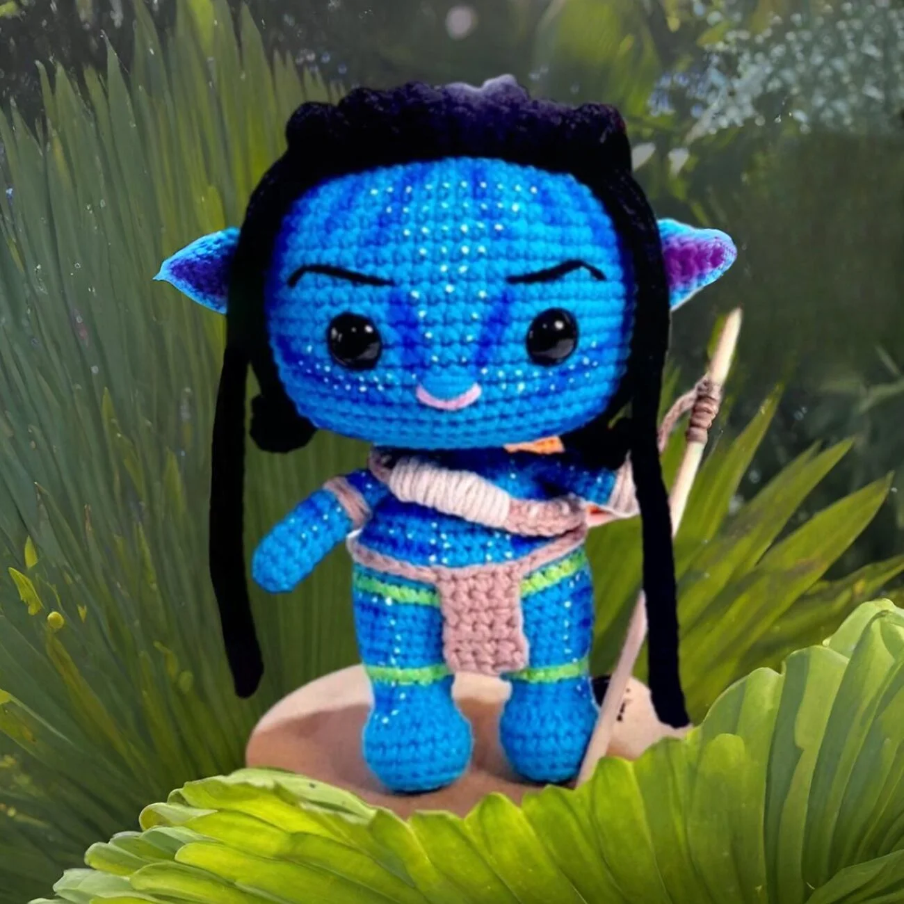 Muñeco amigurumi de Avatar Na'vi terminado, estilo Funko Pop, con detalles de pintura azul y lanza, tejido a crochet.
