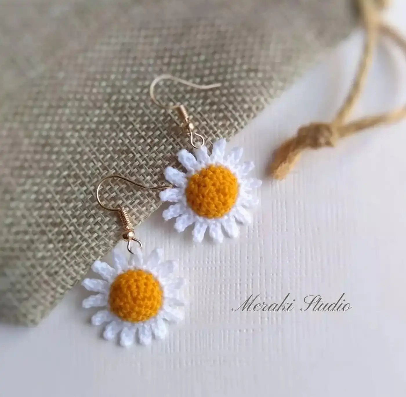 Pendientes de margarita tejidos a crochet mostrados sobre una mano, patrón gratis paso a paso