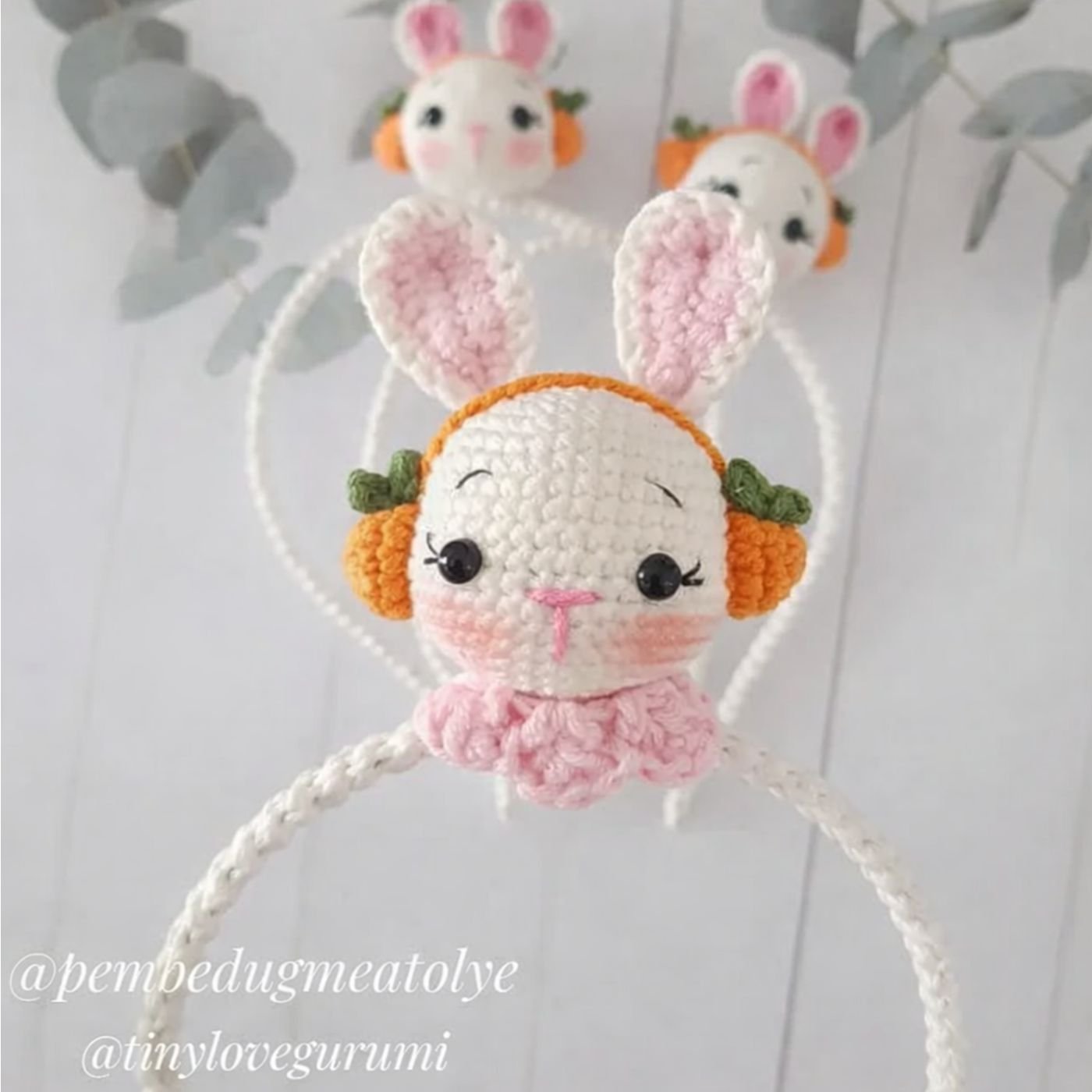 Diadema de crochet con cabeza de conejo amigurumi, orejeras de zanahoria y detalles en rosa.