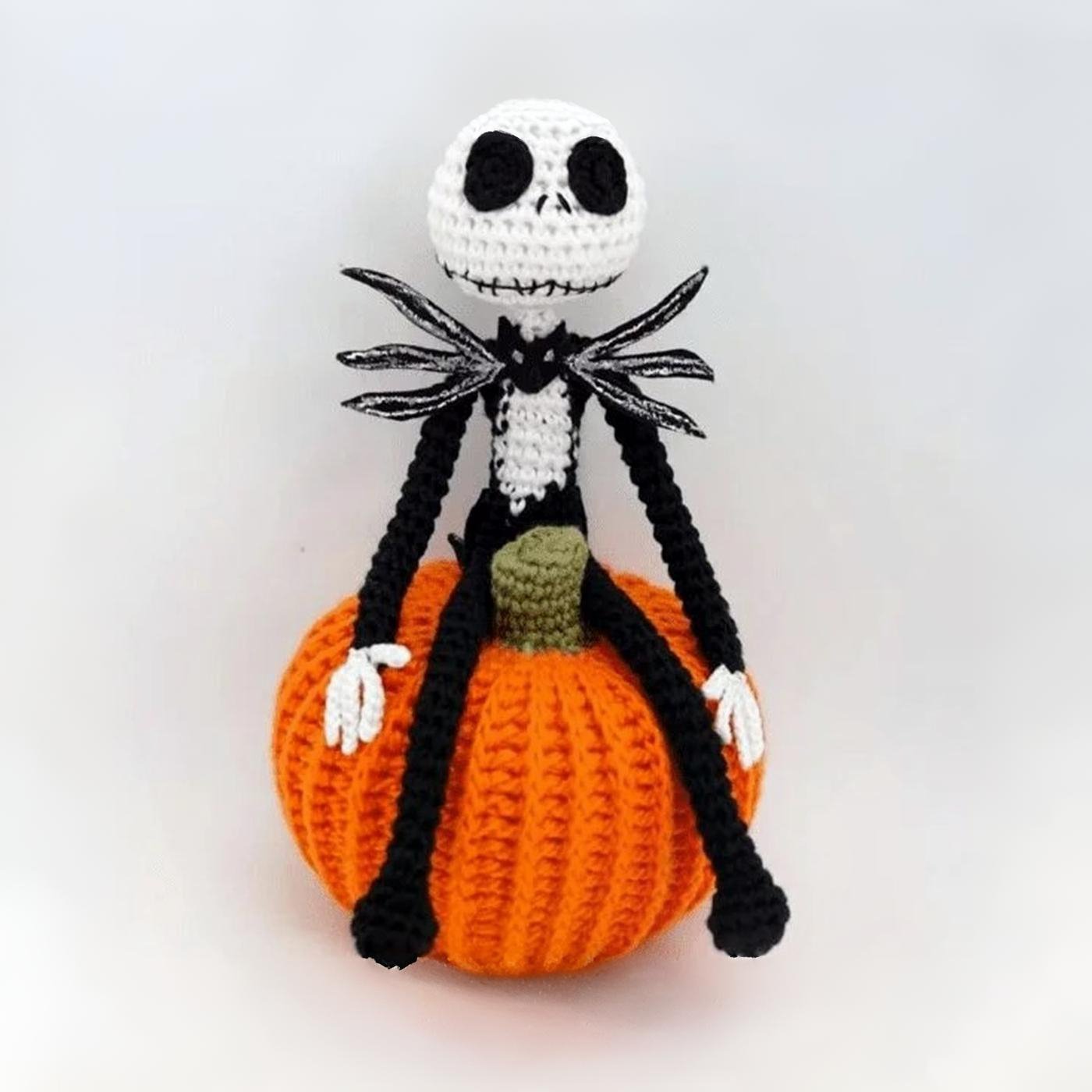 Amigurumi de Jack Skellington con traje negro sentado sobre una calabaza naranja tejida a crochet sobre fondo blanco.