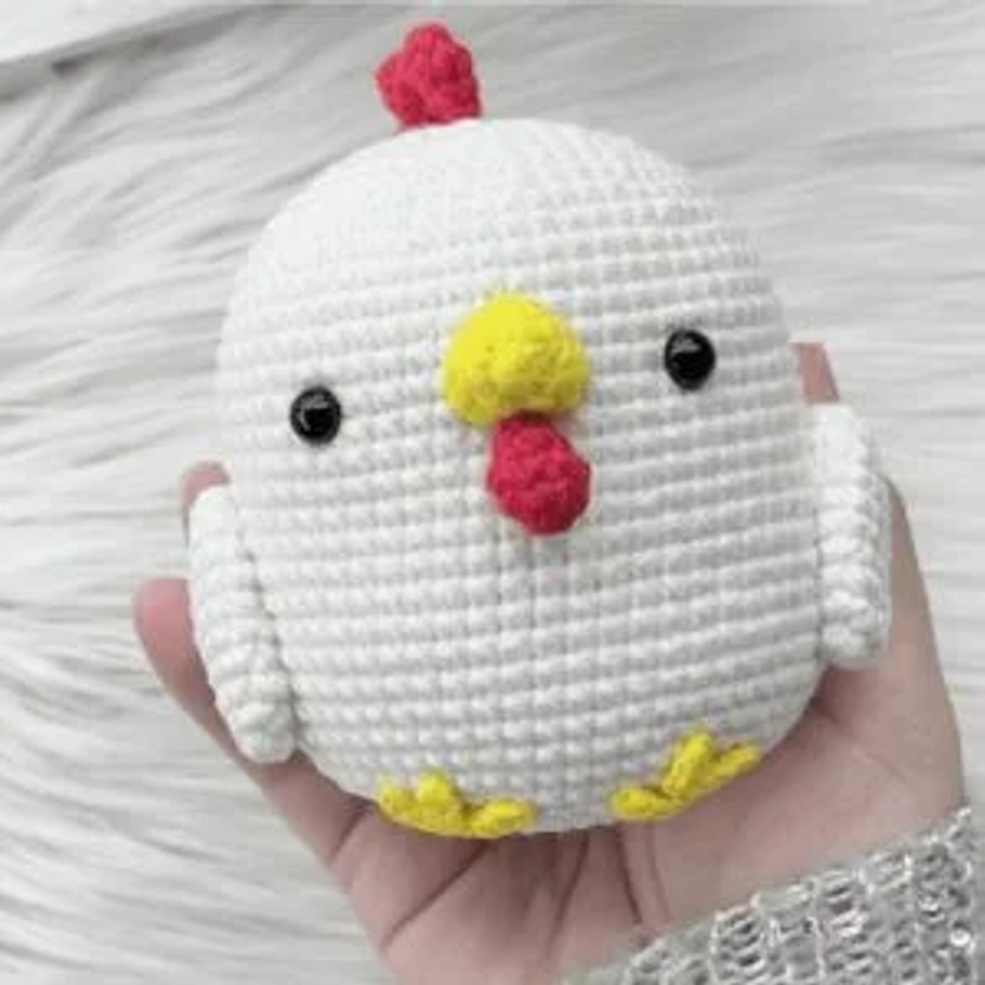Pequeño pollito de amigurumi color blanco con pico amarillo y cresta roja, sostenido en la palma de una mano.