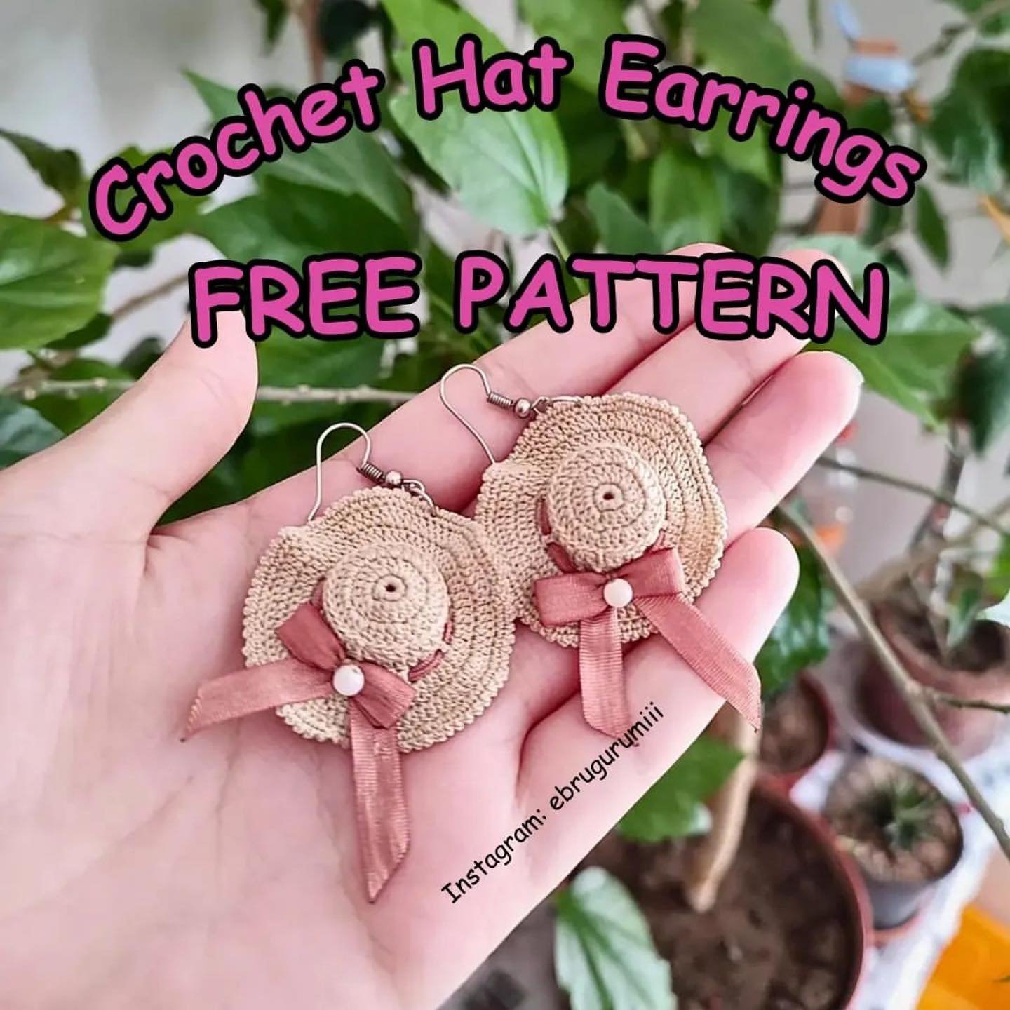 Par de pendientes tejidos a crochet con forma de sombreros de paja decorados con lazos rosados sobre una mano abierta.