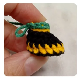 Mano sosteniendo un pequeño zapato tejido a ganchillo con hilos negro, amarillo y verde.