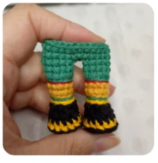 Mano sosteniendo unos pantalones tejidos a ganchillo de colores verde, amarillo, rojo y negro para un amigurumi.