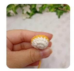 Mano sosteniendo una pequeña pieza de crochet blanca y amarilla para el amigurumi Zayu.