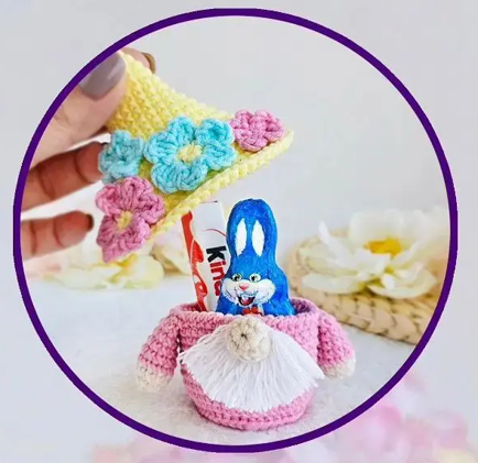 Gnomo tejido de ganchillo en color rosa que sostiene un conejo de chocolate Kinder en su interior.