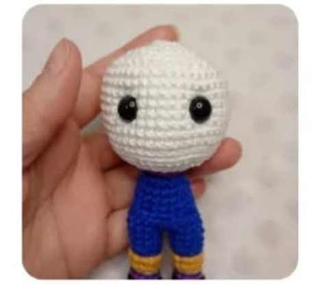 Mano sosteniendo una figura amigurumi tejida a ganchillo con cabeza blanca redonda y cuerpo azul.