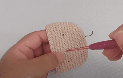 Primer plano de manos tejiendo un amigurumi beige de Don Ramón.