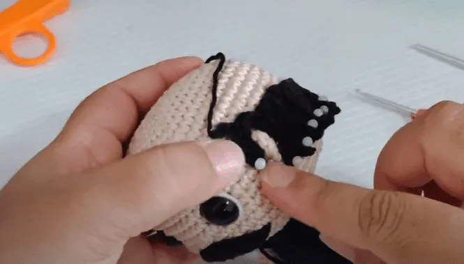 Primer plano de manos tejiendo una oreja amigurumi de Don Ramón.